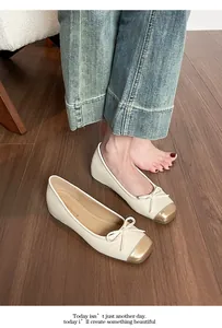 Eleganti ballerine crema con punta dorata e fiocco mostrate su un pavimento in legno