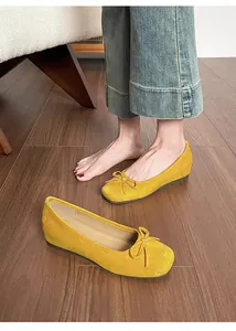 Close-up of yellow suede ballet flats featuring a decorative bow detail on a wooden floor.