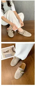 Khaki suede mules with gold buckle strap on wooden floor with lifestyle magazine