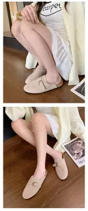 A model wearing beige suede buckle mules with thick soles while sitting on a wooden floor
