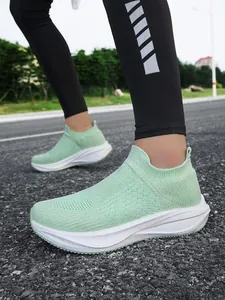 Close-up view of lightweight mint green knit slip-on sneakers on an outdoor road.