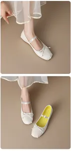 Detailed view of cream white French-style ballet flats featuring a bow and elastic strap