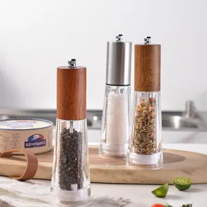 Manual acrylic pepper grinder set with solid wood and stainless steel lids on wooden board.
