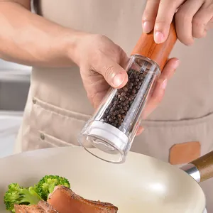 Manual acrylic pepper grinder with ergonomic wooden top being used over a frying pan