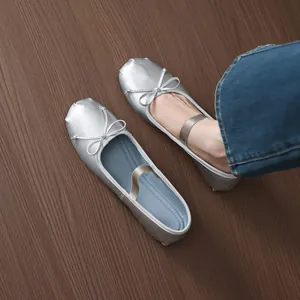 Elegant silver ballet flats featuring a delicate bow and elastic strap on wooden floor