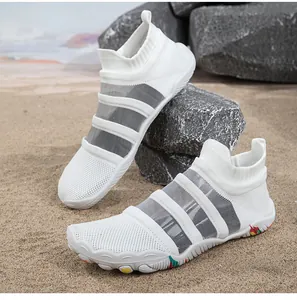 Detailed view of white breathable mesh water shoes on beach sand with scenic stones.