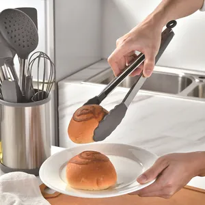 12-piece grey silicone kitchen utensil set with tongs picking up a bun on a plate.