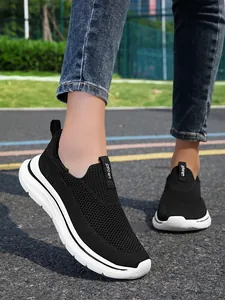 Zapatillas de deporte sin cordones de punto negro transpirable para mujer con suela blanca.