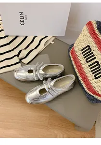 Nahaufnahme silberner Mary Jane Ballerinas mit Klettverschluss auf einer Bank.