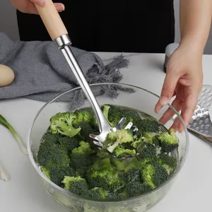 Stainless steel pasta server with wooden handle scooping broccoli from a glass bowl.