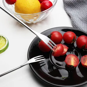 Modern stainless steel fruit forks for appetizers dessert on a black ceramic plate with food