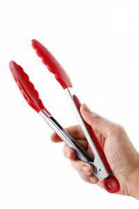 Close-up of stainless steel kitchen tongs with red silicone grip being held by hand.
