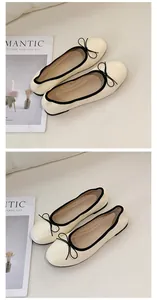 Elegante cremefarbene Ballerinas mit schwarzem Rand und Schleifendetail auf neutralem Grund.