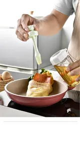 Silicone oil brush drizzling oil onto food in a pink frying pan, kitchen detail