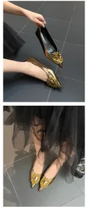 Detailed view of metallic gold pointed-toe flat shoes with an ornate golden buckle.