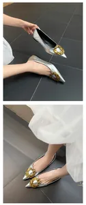 Detailed view of silver pointed toe flats with large hammered gold buckle decoration