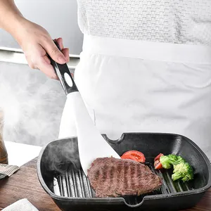 Espátula de silicona blanca volteando un filete a la parrilla en sartén con brócoli.