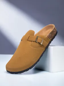 Gros plan de sabots en daim camel avec boucle métallique réglable et détail de semelle en liège.