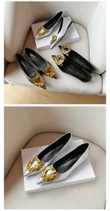 Detail view of silver pointed-toe flat shoes featuring a large gold textured metal buckle