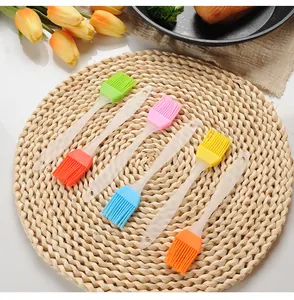 Six colorful silicone basting brushes with translucent handles displayed on a rustic woven mat
