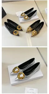 Close-up detail of pointed-toe flats featuring a large textured golden buckle ornament