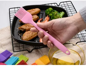 Small pink silicone basting brush held over grilled food with various color options shown