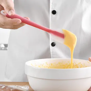 Small pink translucent silicone spatula for baking and cream scraping in a chef's hand.