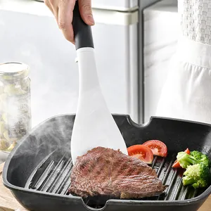 Espátula de silicona profesional volteando un filete en una sartén con verduras.