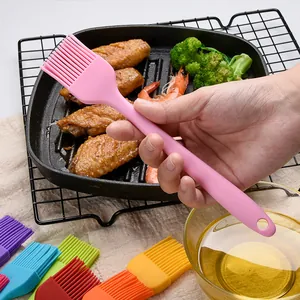 Pink silicone basting brush held over a grill pan with chicken wings and a bowl of oil