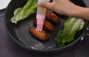 Détail d'un pinceau à huile en silicone rose appliquant de l'huile sur des ailes de poulet