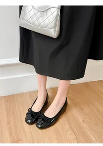 Close-up of black patent leather ballet flats with a delicate bow worn by a model