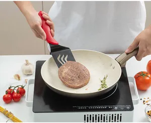 Detail view of a long kitchen spatula with an ergonomic red handle flipping a meat patty