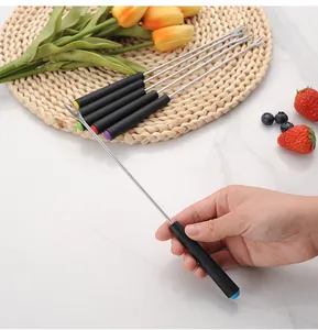 Detailed view of a long stainless steel fondue fork with black handle held by hand.