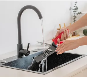 Easy-clean black pizza peel with red handle being washed under a kitchen faucet in sink