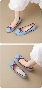 Detailed view of light blue suede ballet flats featuring a red bow and low block heel