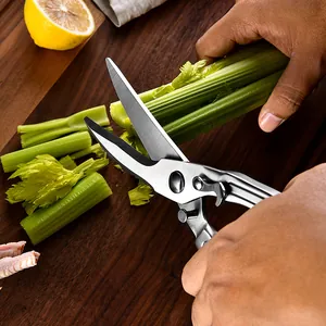 Professional heavy-duty stainless steel kitchen shears cutting fresh celery on a wooden board.