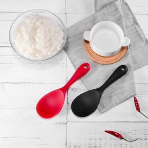 Set of non-stick silicone rice spoons in red and black on a rustic white wood table