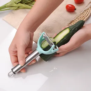 Dual-head stainless steel vegetable peeler and grater tool in use for cucumber