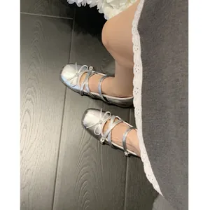 Elegant silver ballet flats featuring a decorative bow and straps on a dark wood floor