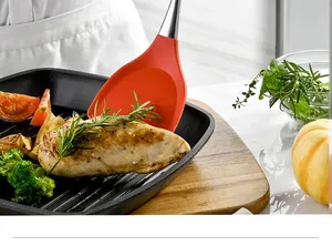 A close-up shot of a red silicone spatula flipping grilled chicken in a non-stick pan
