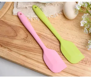 Detail of pink and lime green silicone cream spatulas for baking on a wooden board.