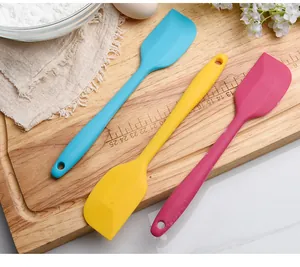 Detail view of colorful silicone spatulas on a wooden board with baking props