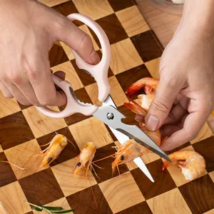 Pink stainless steel kitchen scissors cutting fresh shrimp on a checkered board.