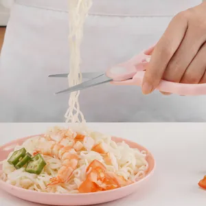 Tijeras para comida de bebé de acero inoxidable rosa cortando fideos sobre un plato