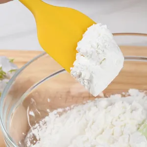 Yellow silicone kitchen spatula scraper picking up flour in a glass bowl for baking.
