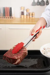 Detailed close-up of silicone food tongs gripping a seasoned steak over a grill pan