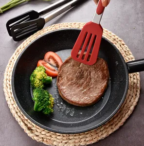 Close-up of red silicone tipped kitchen tongs flipping a juicy steak in a frying pan