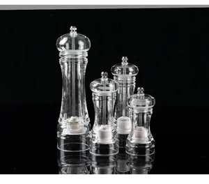 Set of four clear acrylic spice grinders in various heights on a black reflective background.