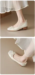 Detail view of cream French ballet flats with bow and block heel paired with a pleated skirt