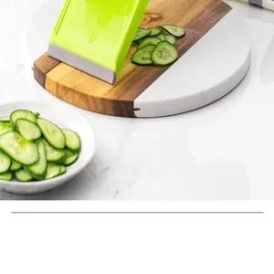 Handheld vegetable mandoline slicer cutting fresh cucumber slices on a marble board